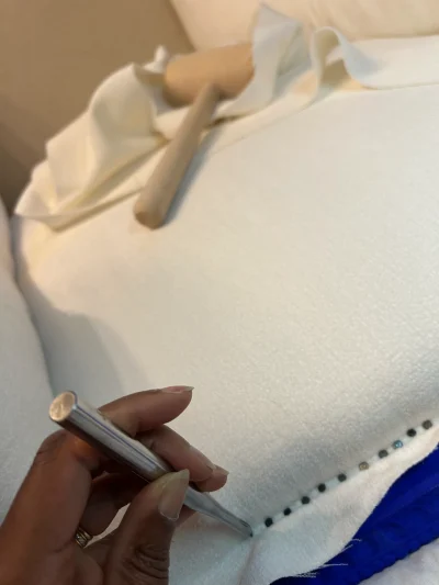 Main de Sylvie Picard en train de posé des clous pour tapisser l'assise d'un fauteuil